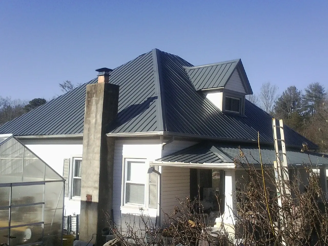 Dark blue standing seam metal roof on a white farmhouse with dormer — Slate & Tile Roof Repair by Roofing Brothers in Hilham