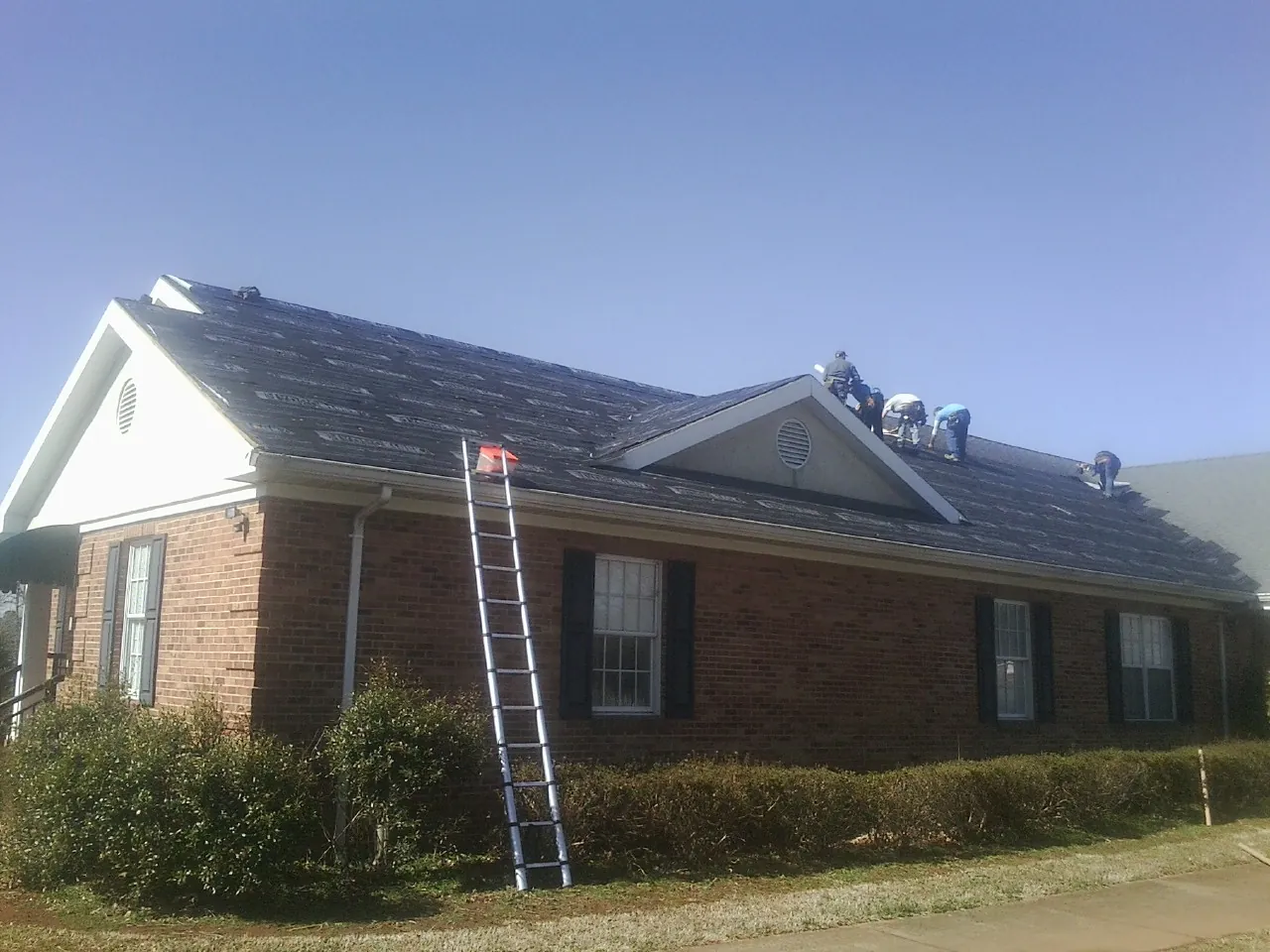 Crew tearing shingles off a brick ranch roof with a ladder set — Emergency Roof Repair work by our crew in Hilham