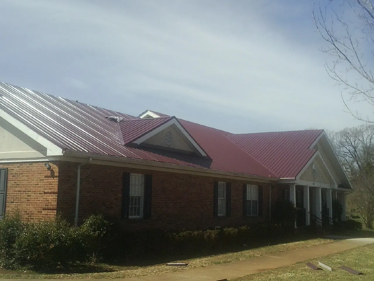 Red metal roof with gabled entries on a long brick building, from a Hail Damage Roof Repair job in Hilham