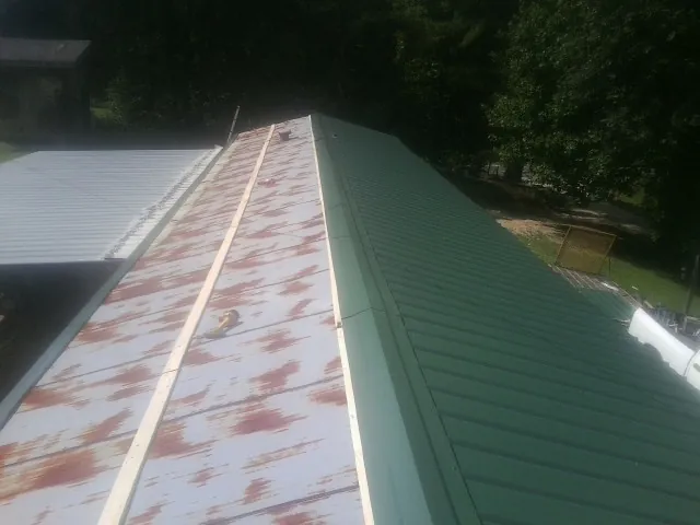 Old rusted panels beside newly installed green metal roofing — Wind Damage Roof Repair by Roofing Brothers in Hilham