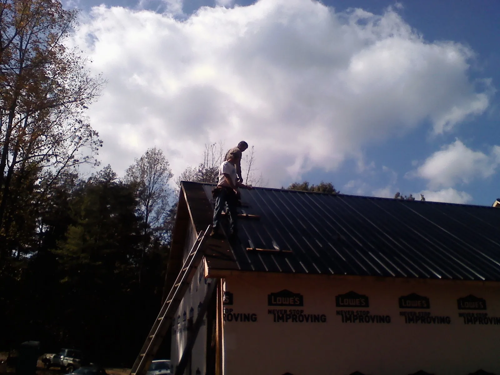 Roofer fastening dark metal panels high against a cloudy sky, from a Roof Inspection job in Hilham