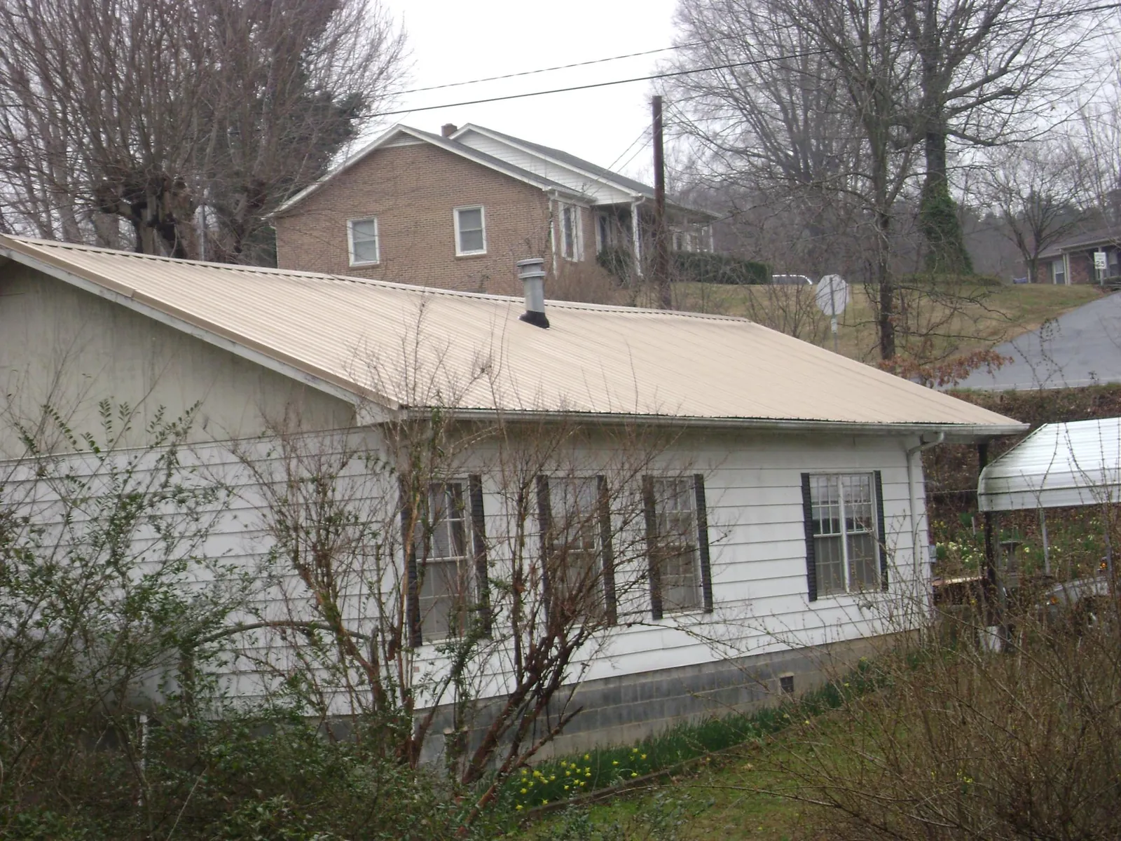Tan metal roof on a white sided house set into a hillside — Commercial Roofing by Roofing Brothers in Hilham