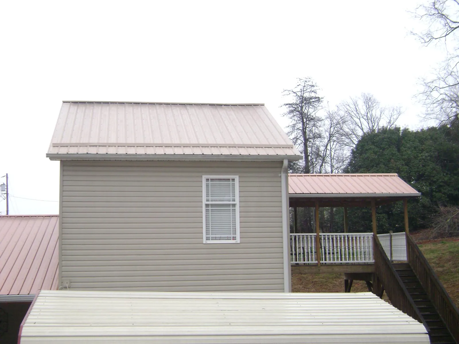 Tan metal roofs on a two story addition and attached porch, from a Roof Replacement job in Hilham